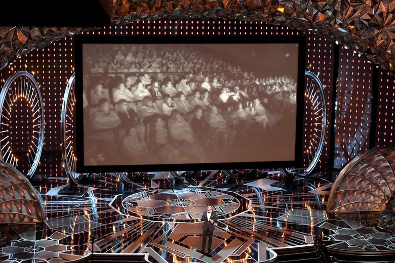 Host Jimmy Kimmel speaks onstage in front of a projection of another movie screening elsewhere.